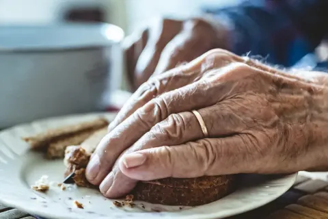 Abbildung von Händen einer älteren Person, welche ein Stück Brot halbiert.